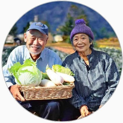 収穫した野菜を持ち畑に座る笑顔の老夫婦
